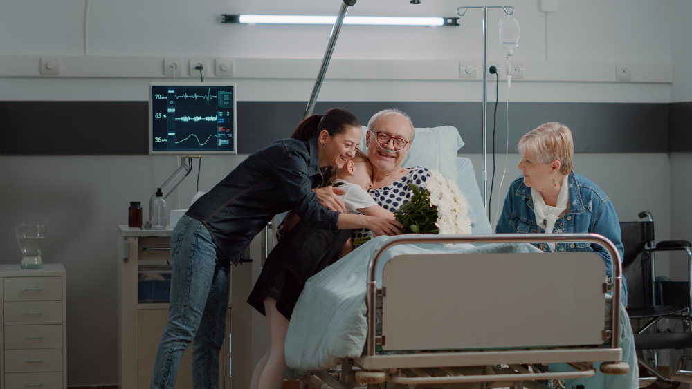 aged man in emergeny room visits on a bed surround by family