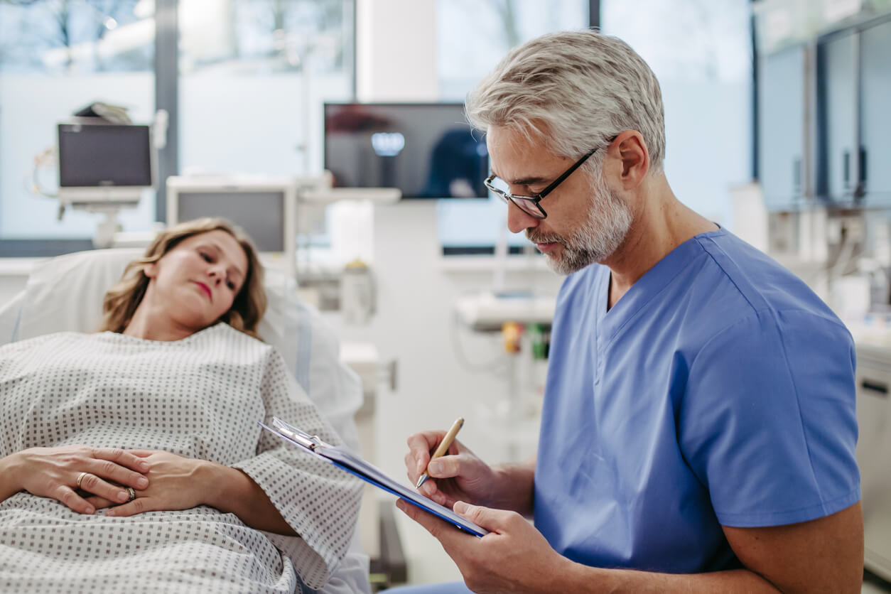 Doctor talking with worried patient before surgery, writing medical document.